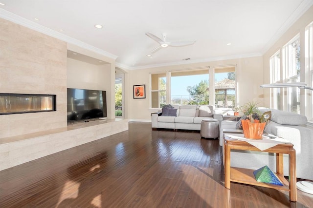 living room with ceiling fan, hardwood / wood-style floors, ornamental molding, and a tiled fireplace