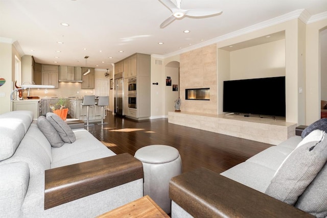 living room with wood-type flooring, a tile fireplace, ceiling fan, and ornamental molding