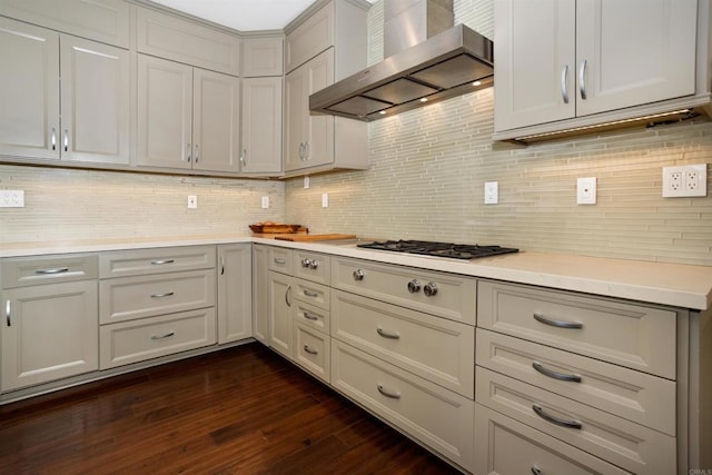 kitchen with tasteful backsplash, dark wood-style floors, wall chimney exhaust hood, light countertops, and stainless steel gas cooktop