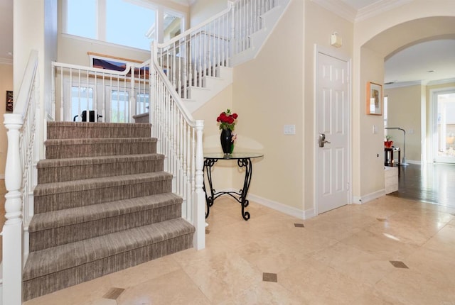 stairs featuring crown molding, a high ceiling, arched walkways, and baseboards