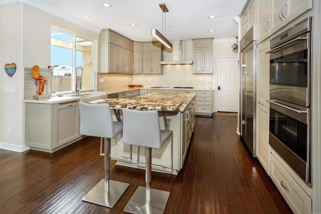 kitchen with a sink, backsplash, a center island, appliances with stainless steel finishes, and wall chimney exhaust hood