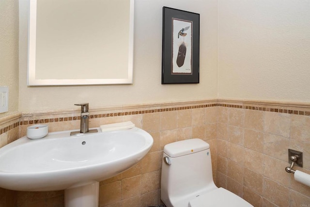 bathroom with wainscoting, toilet, tile walls, and a sink