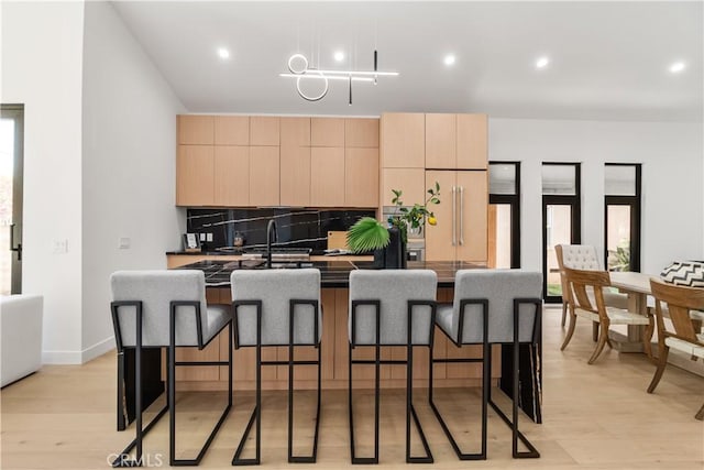 kitchen with decorative backsplash, an island with sink, light brown cabinetry, modern cabinets, and light wood finished floors