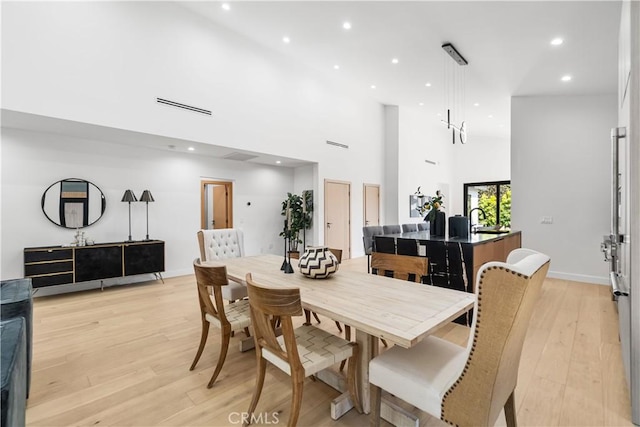 dining area featuring a high ceiling, light wood finished floors, baseboards, visible vents, and recessed lighting
