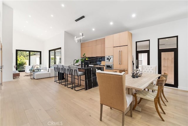 dining room featuring baseboards, light wood-style flooring, a high ceiling, and recessed lighting