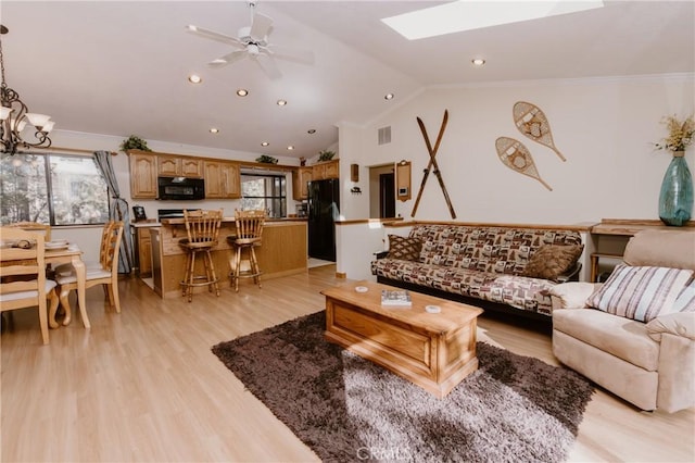 living room featuring ceiling fan with notable chandelier, crown molding, light hardwood / wood-style floors, and vaulted ceiling with skylight