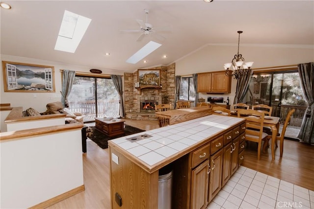 kitchen featuring pendant lighting, a stone fireplace, light hardwood / wood-style floors, tile countertops, and vaulted ceiling