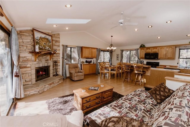 living room featuring ceiling fan with notable chandelier, light hardwood / wood-style floors, a fireplace, and vaulted ceiling with skylight