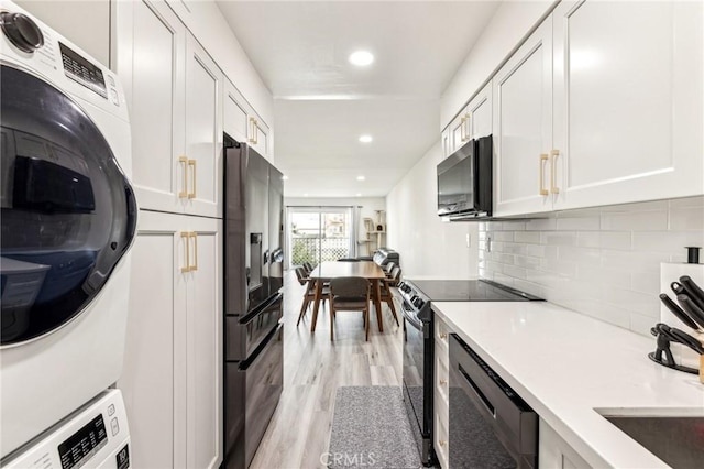 kitchen featuring white cabinetry, black appliances, and stacked washer and clothes dryer