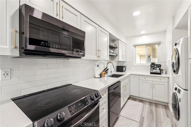 kitchen with stacked washer / dryer, white cabinets, dishwasher, sink, and stainless steel electric range