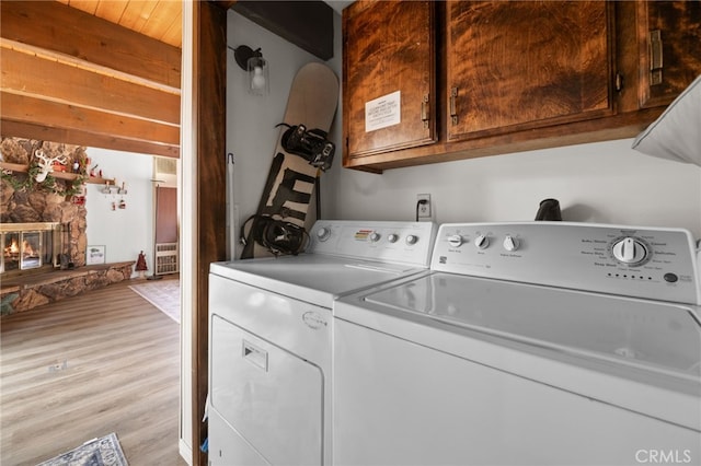 laundry room with cabinets, a stone fireplace, light wood-type flooring, and washer and clothes dryer