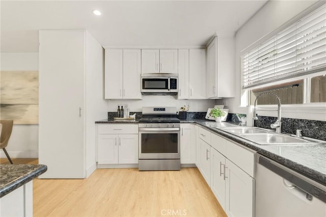 kitchen featuring appliances with stainless steel finishes, sink, white cabinets, light wood-type flooring, and dark stone countertops