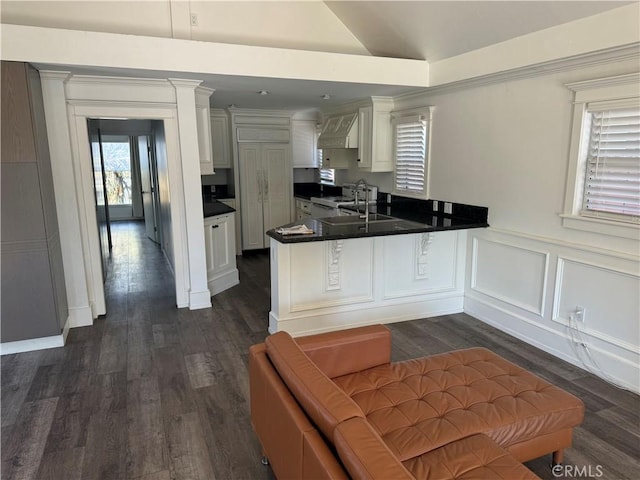 kitchen featuring lofted ceiling, wall chimney exhaust hood, white cabinets, and kitchen peninsula