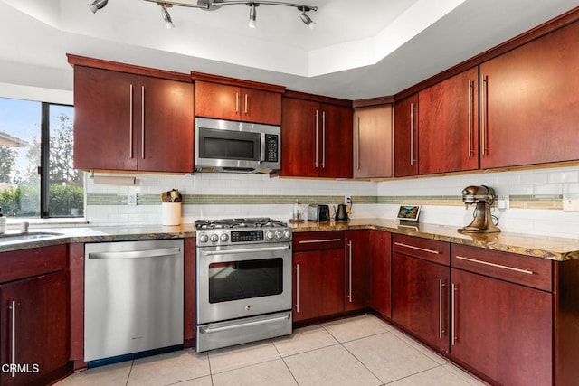 kitchen with stainless steel appliances, a raised ceiling, light tile patterned floors, and decorative backsplash