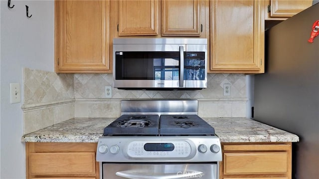 kitchen featuring stainless steel appliances, light stone countertops, and decorative backsplash