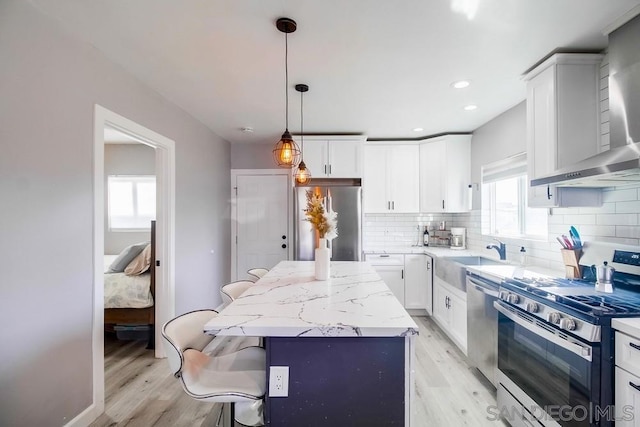 kitchen featuring white cabinetry, stainless steel appliances, a kitchen island, decorative light fixtures, and wall chimney exhaust hood