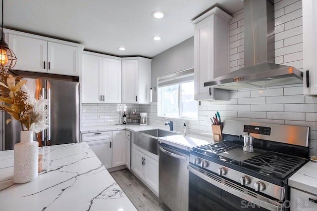 kitchen with decorative light fixtures, white cabinets, light stone counters, stainless steel appliances, and wall chimney range hood