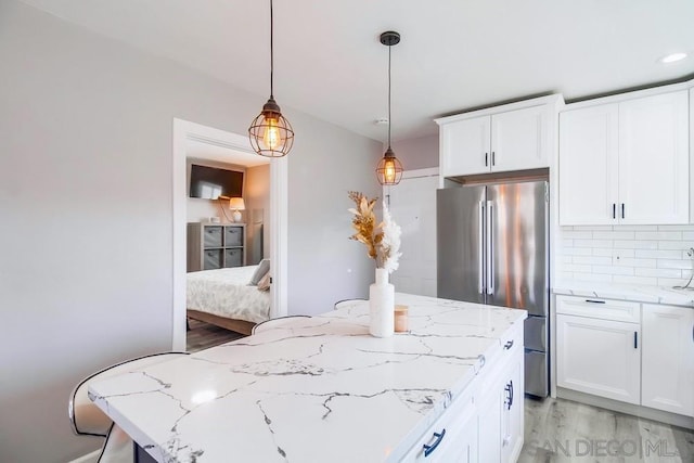 kitchen with white cabinetry, decorative light fixtures, stainless steel fridge, light stone countertops, and decorative backsplash