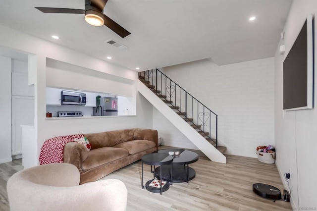 living room with light hardwood / wood-style floors, brick wall, and ceiling fan