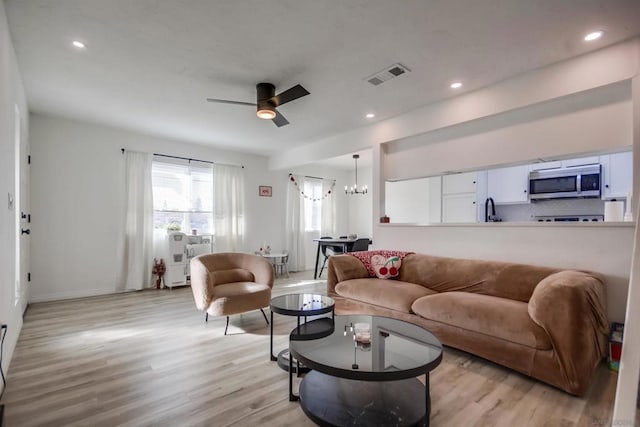 living room with sink, light hardwood / wood-style floors, and ceiling fan with notable chandelier