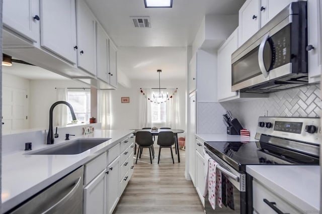 kitchen with white cabinets, appliances with stainless steel finishes, decorative light fixtures, tasteful backsplash, and sink