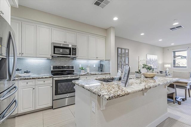 kitchen with stainless steel appliances, a kitchen island with sink, sink, and white cabinets