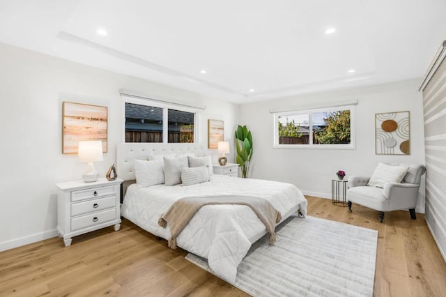 bedroom with light hardwood / wood-style flooring and a raised ceiling