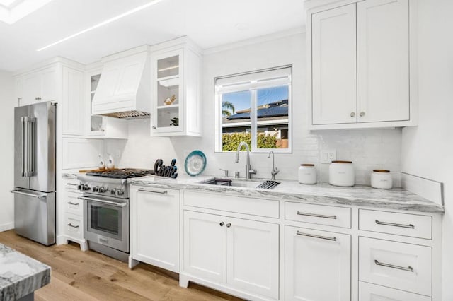 kitchen featuring premium range hood, white cabinetry, sink, high end appliances, and light stone countertops