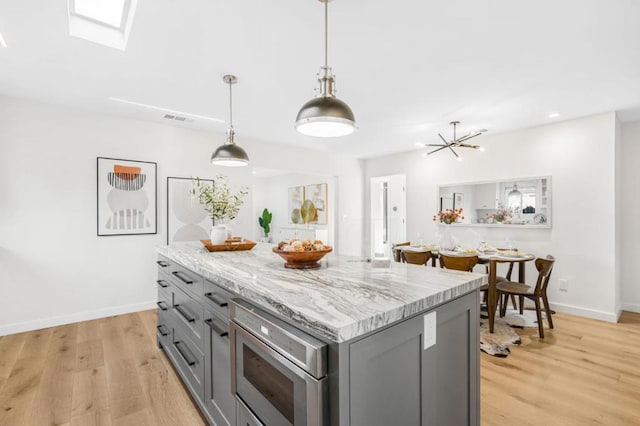 kitchen with a kitchen island, stainless steel microwave, gray cabinetry, hanging light fixtures, and light stone counters