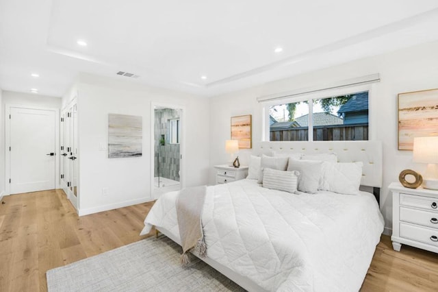 bedroom with a tray ceiling and light wood-type flooring