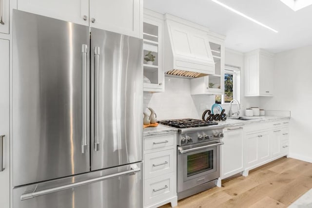 kitchen with white cabinetry, sink, light stone counters, and high quality appliances