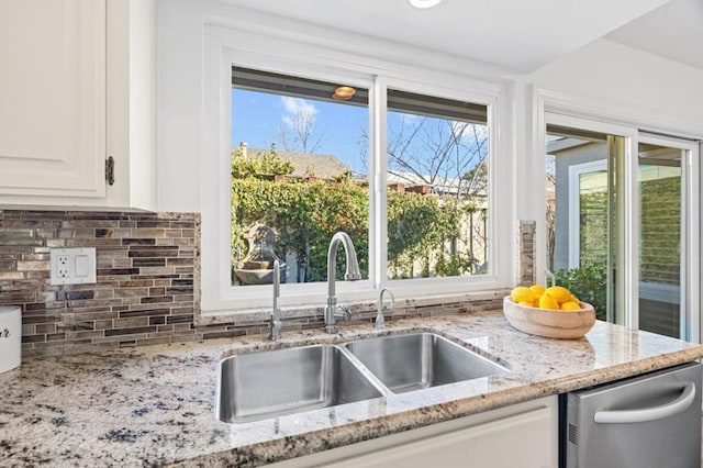 kitchen featuring light stone countertops, tasteful backsplash, white cabinetry, stainless steel dishwasher, and sink