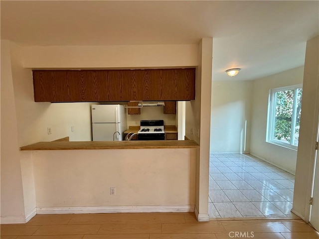 kitchen featuring kitchen peninsula, white refrigerator, gas range oven, and light tile patterned flooring