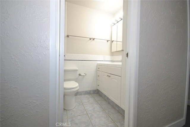 bathroom featuring toilet, vanity, tile patterned floors, and tile walls