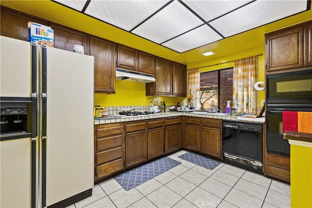 kitchen featuring sink, light tile patterned floors, black appliances, and tile counters