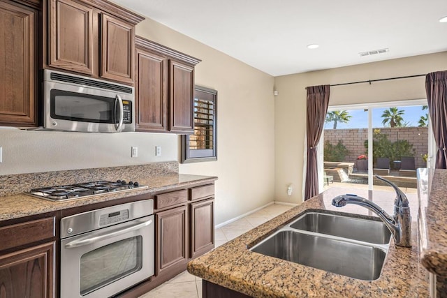 kitchen with sink, light tile patterned flooring, light stone counters, and stainless steel appliances