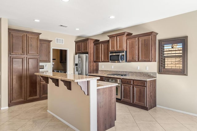 kitchen with a kitchen bar, light stone countertops, appliances with stainless steel finishes, a kitchen island, and light tile patterned flooring