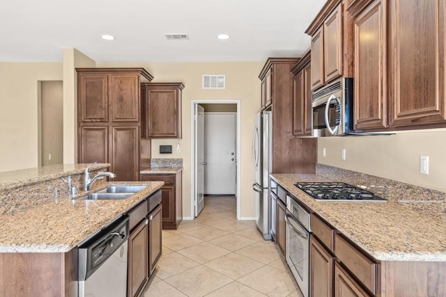 kitchen featuring sink, light stone countertops, light tile patterned flooring, an island with sink, and stainless steel appliances