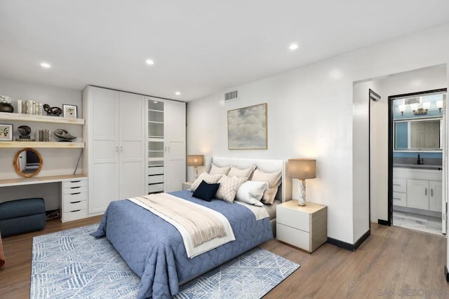 bedroom featuring sink, built in desk, connected bathroom, and hardwood / wood-style floors