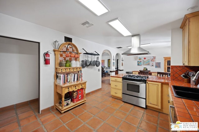 kitchen featuring light brown cabinetry, tile counters, stainless steel gas range, island exhaust hood, and sink