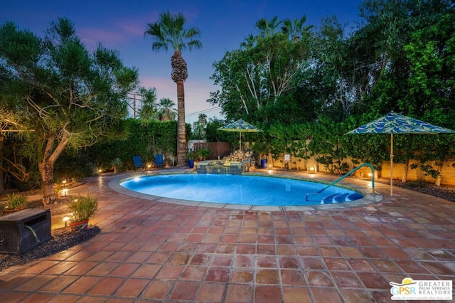 pool at dusk featuring a patio and pool water feature