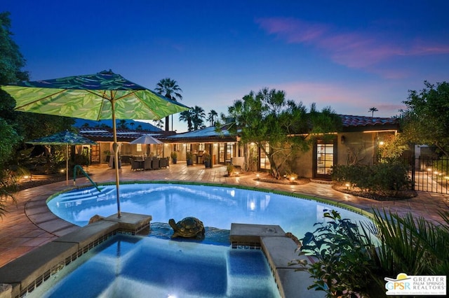 pool at dusk featuring a patio area and a jacuzzi