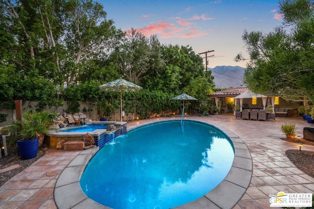 pool at dusk featuring an in ground hot tub, pool water feature, and a patio