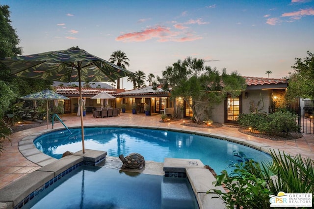 pool at dusk featuring a patio area and a hot tub