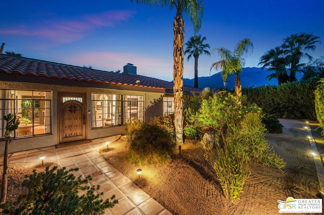 exterior entry at dusk with a mountain view and a patio area