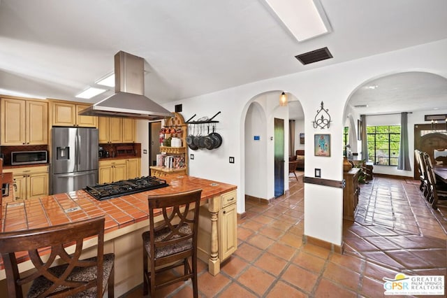 kitchen with appliances with stainless steel finishes, tile patterned floors, tasteful backsplash, island range hood, and tile countertops