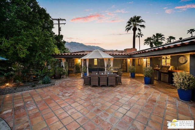 patio terrace at dusk featuring exterior kitchen, grilling area, and a mountain view