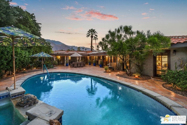 pool at dusk with a mountain view and a patio area