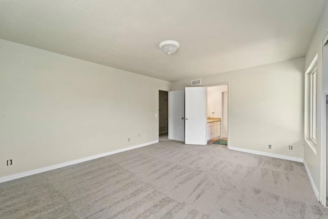 unfurnished bedroom featuring light colored carpet and ensuite bath