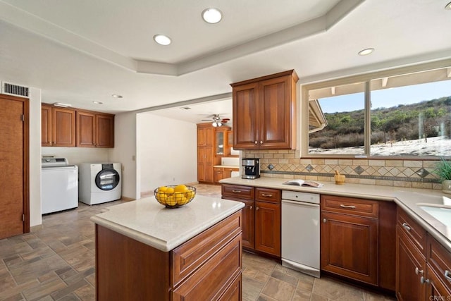 kitchen featuring separate washer and dryer, a center island, decorative backsplash, ceiling fan, and a tray ceiling